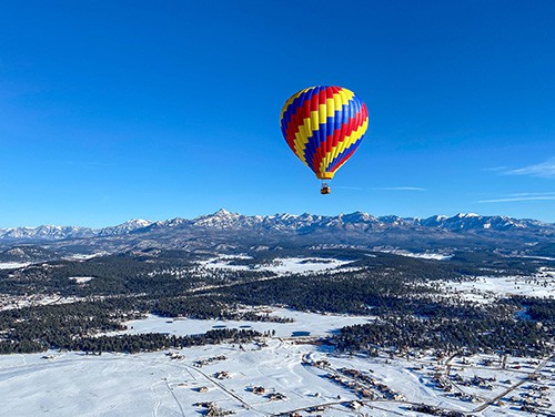 hot air balloon flying above snowy mountains