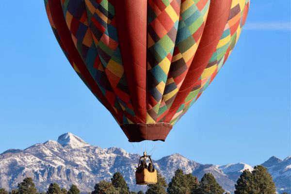 A hot air balloon floating in the sky with snowy mountains behind.