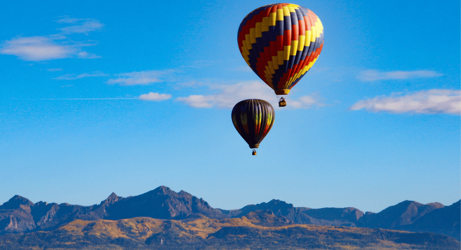 Hot air balloons floating in blue skies with mountains in background.