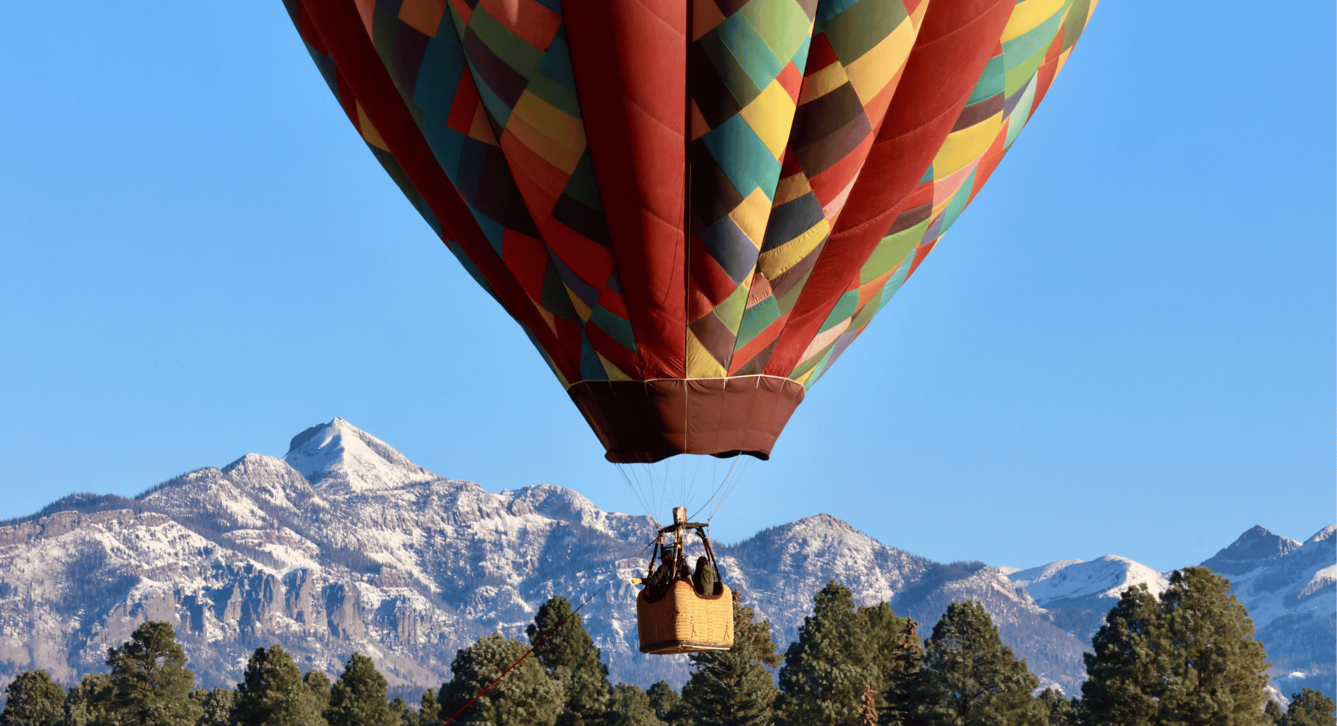 Hot air balloon floating over a field with snowy mountains in background.