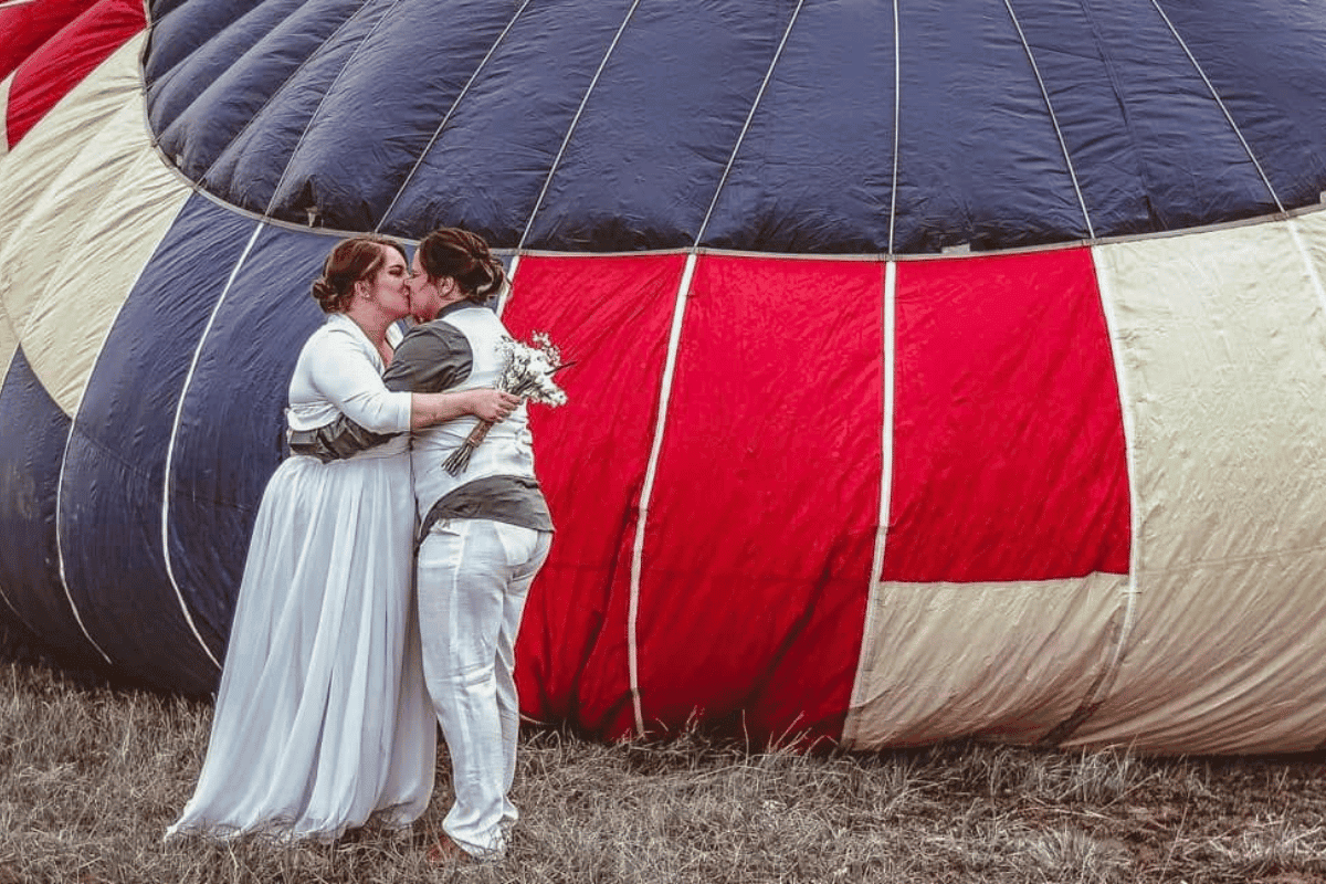 A couple kissing in front of a hot air balloon.