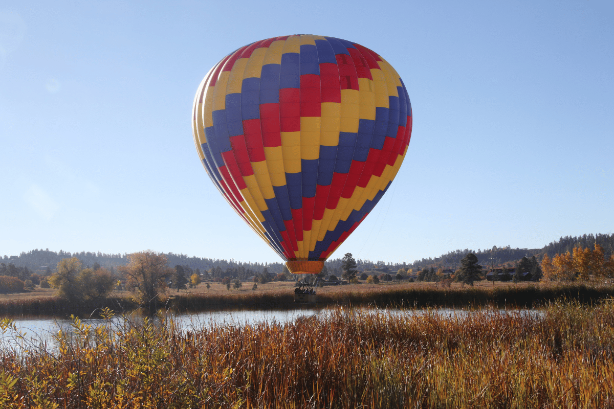 A hot air balloon close to a ponds surface.