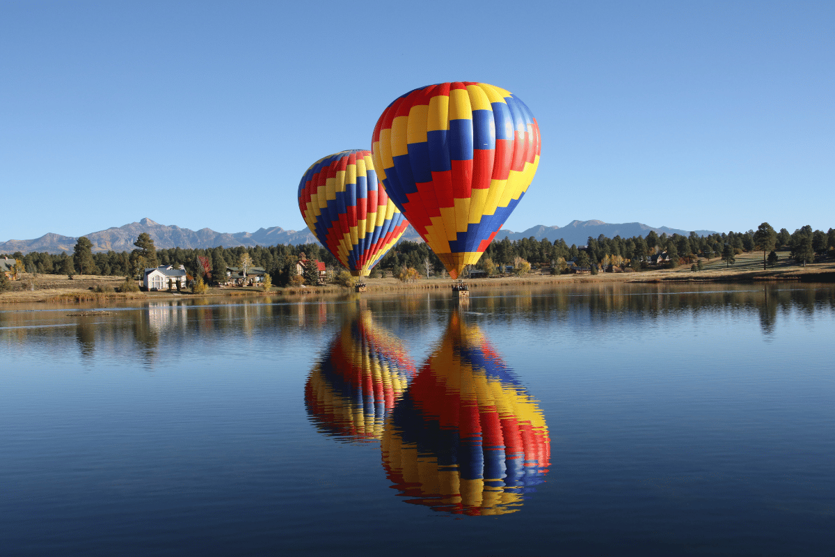 Two hot air balloons flying over surface of a lake.
