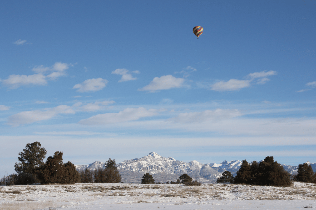 A hot air balloon flying over snowy mountains and field.